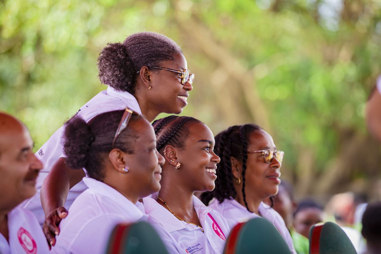 A smiling audience in Peace and Love Hospitals polo shirts watching an outreach event